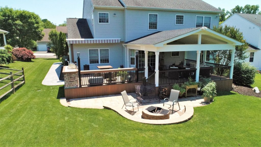 Aerial view of a gabled roof structure over a deck with a paver patio and fire pit