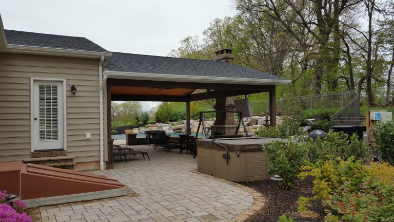 Paver patio leading to an open pavilion with a stone fireplace